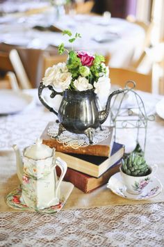 a table topped with books and flowers next to a tea pot on top of a table