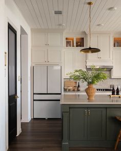 a kitchen with white cabinets and green island in the center is decorated with greenery