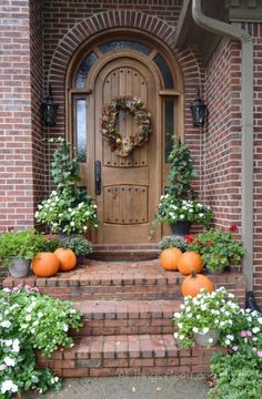 a wooden door surrounded by potted plants and pumpkins in front of a brick house