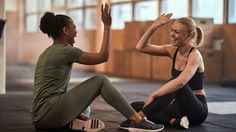 two women sitting on the ground and one is giving high fives to each other