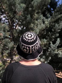 a man wearing a black and white knitted hat standing in front of pine trees