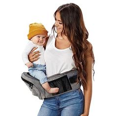 a woman is holding a baby in her back carrier while wearing a hat and jeans