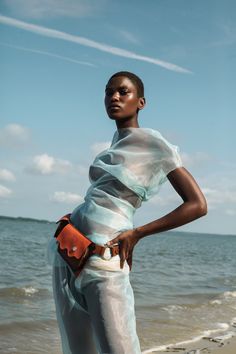 a woman standing on the beach with her hands in her pockets and looking off into the distance