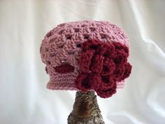 a crocheted pink hat with red flowers on it sitting on top of a metal vase