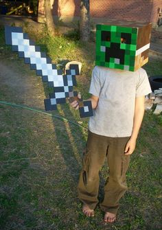 a young boy wearing a minecraft creeper mask standing in front of a house