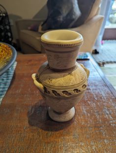 a white vase sitting on top of a wooden table next to a dog in the background