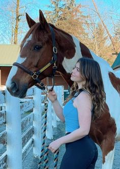 a beautiful young woman standing next to a brown and white horse in a corral