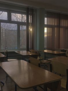 an empty classroom with wooden desks and large windows in the back ground, at dusk