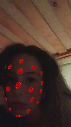 a woman with red lights on her face in front of the camera and behind her is an image of smiley faces