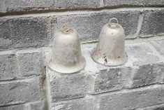 two white bells sitting on the side of a brick wall next to eachother