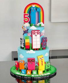 a three tiered cake decorated with cartoon characters and rainbows on the top layer