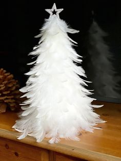 a white feather christmas tree sitting on top of a wooden table next to a pine cone