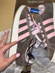 a woman's pink and grey adidas sneaker in a box with her hand on the laces