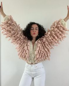 a woman in white pants and a pink jacket with her arms spread out, posing for the camera