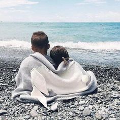 two children wrapped in blankets sitting on the beach