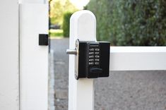 an electronic door lock on a white gate with trees and bushes in the back ground