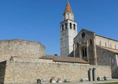 an old stone building with a clock tower in the background and grass on the ground