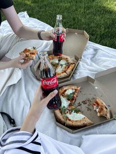 two people eating pizza and drinking coke on a blanket in front of some picnic tables