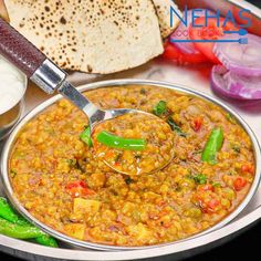 a spoon full of food sitting on top of a metal plate next to bread and vegetables