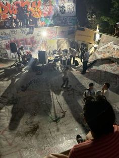 a group of people sitting in front of a wall with graffiti on it at night