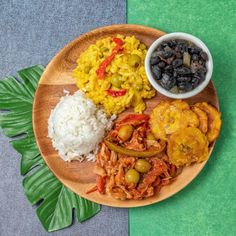 a wooden plate topped with rice, beans and other foods next to a green leaf