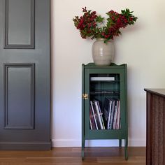 a vase with flowers on top of a green bookcase in front of a door