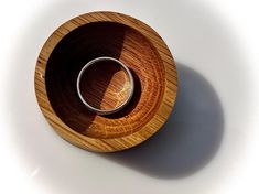 a wooden bowl with a silver ring in it on a white surface, viewed from above