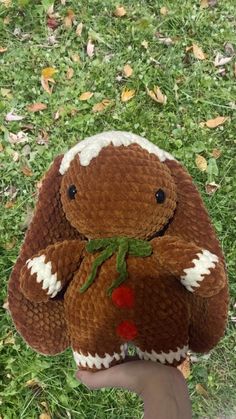 a hand holding a brown and white stuffed animal on top of green grass covered ground