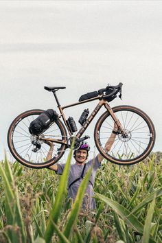 a man standing in a corn field holding his bike up to the camera and smiling