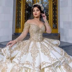 a woman in a gold and white gown standing outside the door of a building with her hand on her head