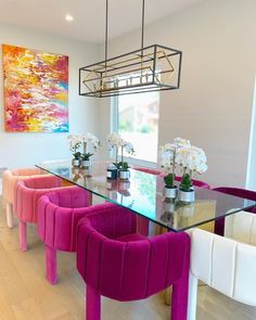 a dining room table with pink chairs and white flowers in vases on the glass top