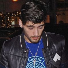 a man in a leather jacket looking down at his cell phone while wearing a blue shirt