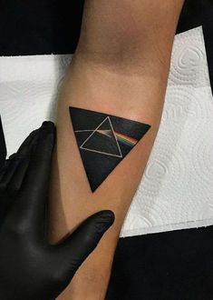 a black triangle tattoo with a rainbow in the middle on someone's left arm