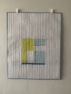 a quilted wall hanging on the side of a white wall with blue and yellow squares