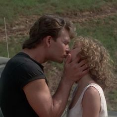 a man kissing a woman on the cheek in front of a car with grass behind him