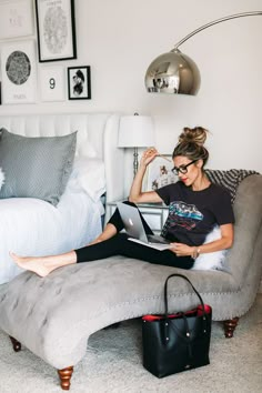 a woman sitting on top of a couch with a laptop computer in her hand and holding a purse