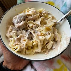 a person is holding a bowl of pasta with meat and cheese on it, while the other hand holds a spoon