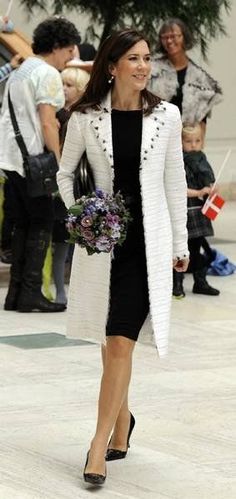 the woman is walking down the street with flowers in her hand and people behind her