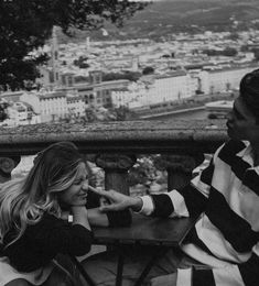 black and white photograph of two people sitting at a table with city in the background