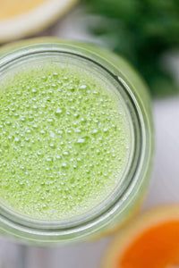 a glass filled with green liquid next to sliced oranges