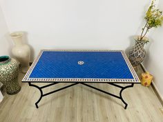 a blue tiled table sitting on top of a hard wood floor next to vases