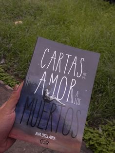 a person holding up a book in front of some grass and bushes with the title cartas de a mor los mierros