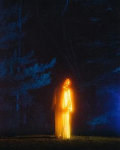 a woman standing in the middle of a forest at night with bright lights shining on her