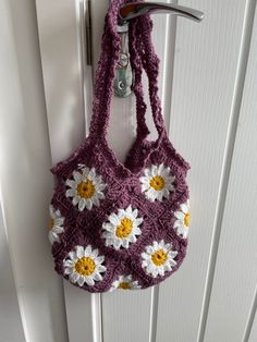 a crocheted purse hanging from a hook on a white door with yellow and white flowers