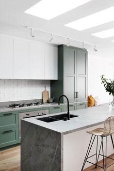 a kitchen with green cabinets and marble counter tops, an island sink and stools