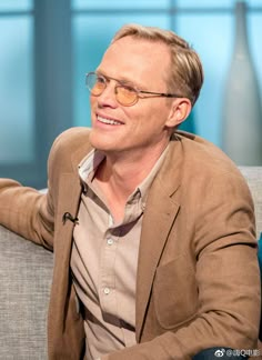 a man sitting on top of a couch in front of a glass window wearing glasses