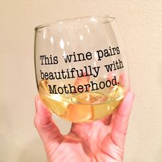 a person holding up a wine glass that says, this wine pairs beautifully with motherhood