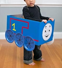 a young boy is wearing a thomas the tank engine costume and holding a cardboard box