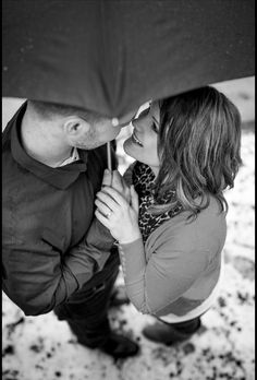 black and white photograph of a couple kissing under an umbrella in the snow with their faces close to each other