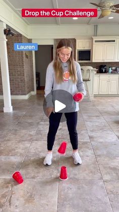 a girl juggling red cups in the middle of a kitchen floor while another girl watches